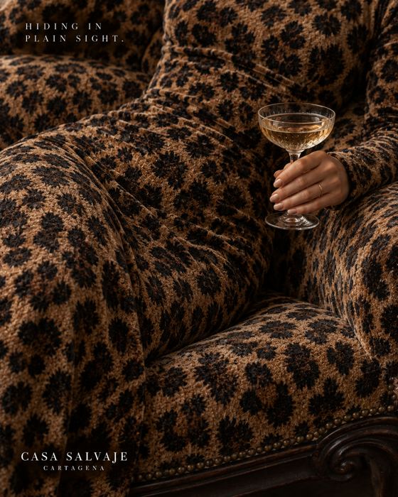 Una mano con una copa sobre un sillón de leopardo